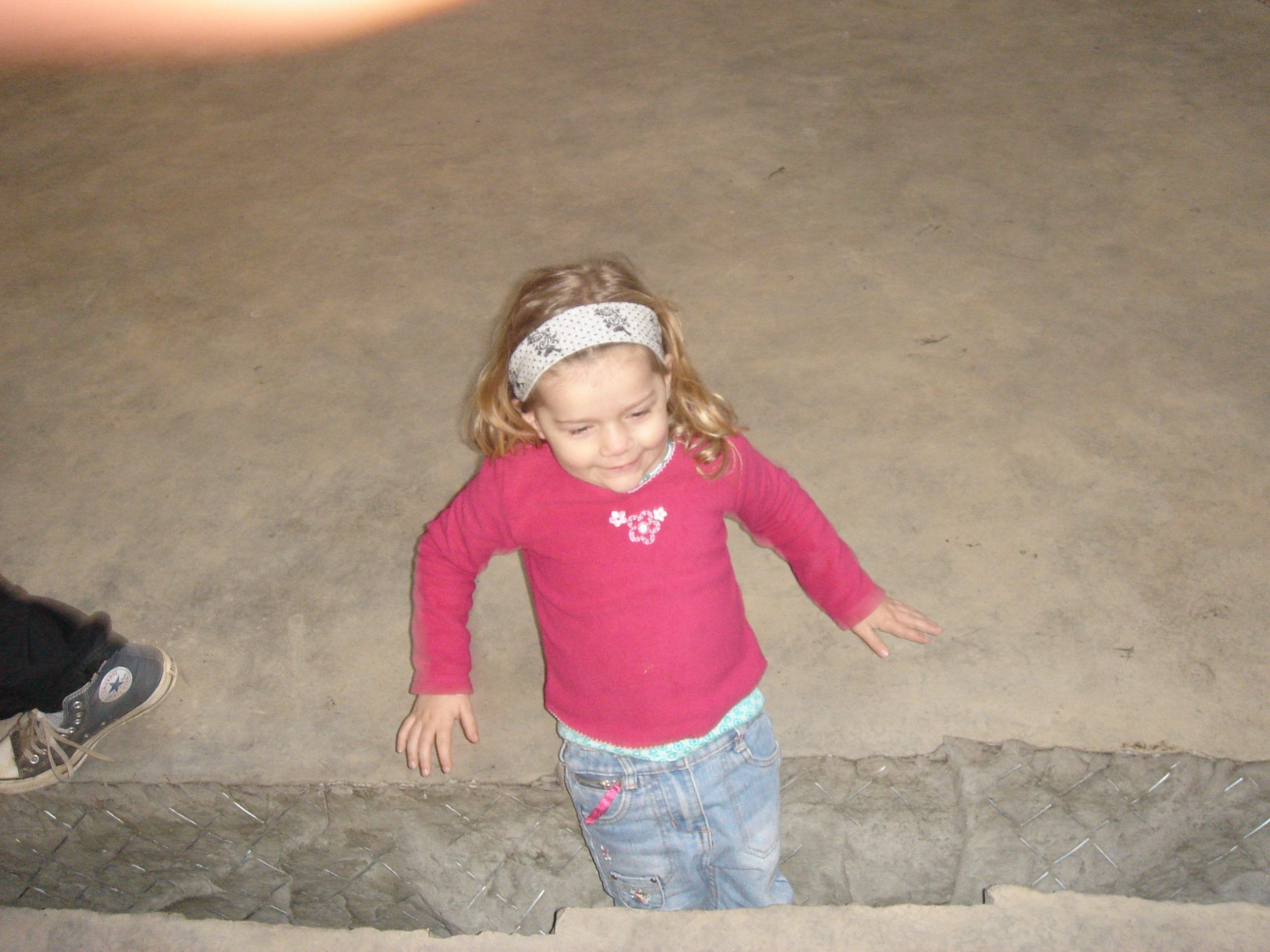 A crack is zigzagging across a concrete floor. A small girl in a pink top is standing in it looking down. It goes up to her knees.