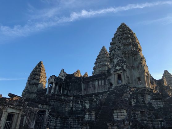A close up of Angkor Wat's highest tower, covered in balconies and  intricate carvings, silhouetted against a bright blue sky.