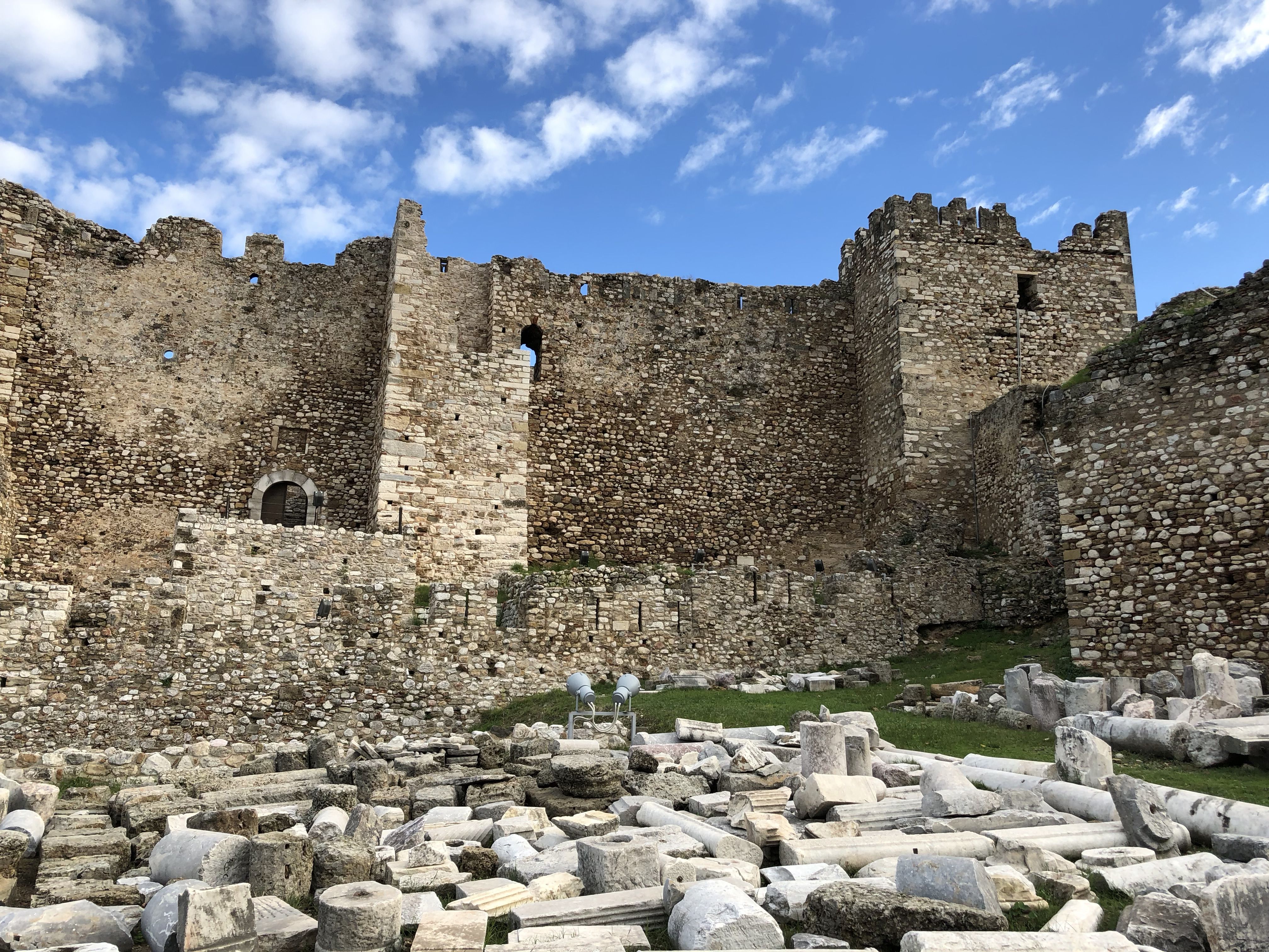 Inside the castle, only the outside walls are standing  and the crenellations on top of the walls are clear. There are small windows and archways, and the remains of some stonework on the ground.