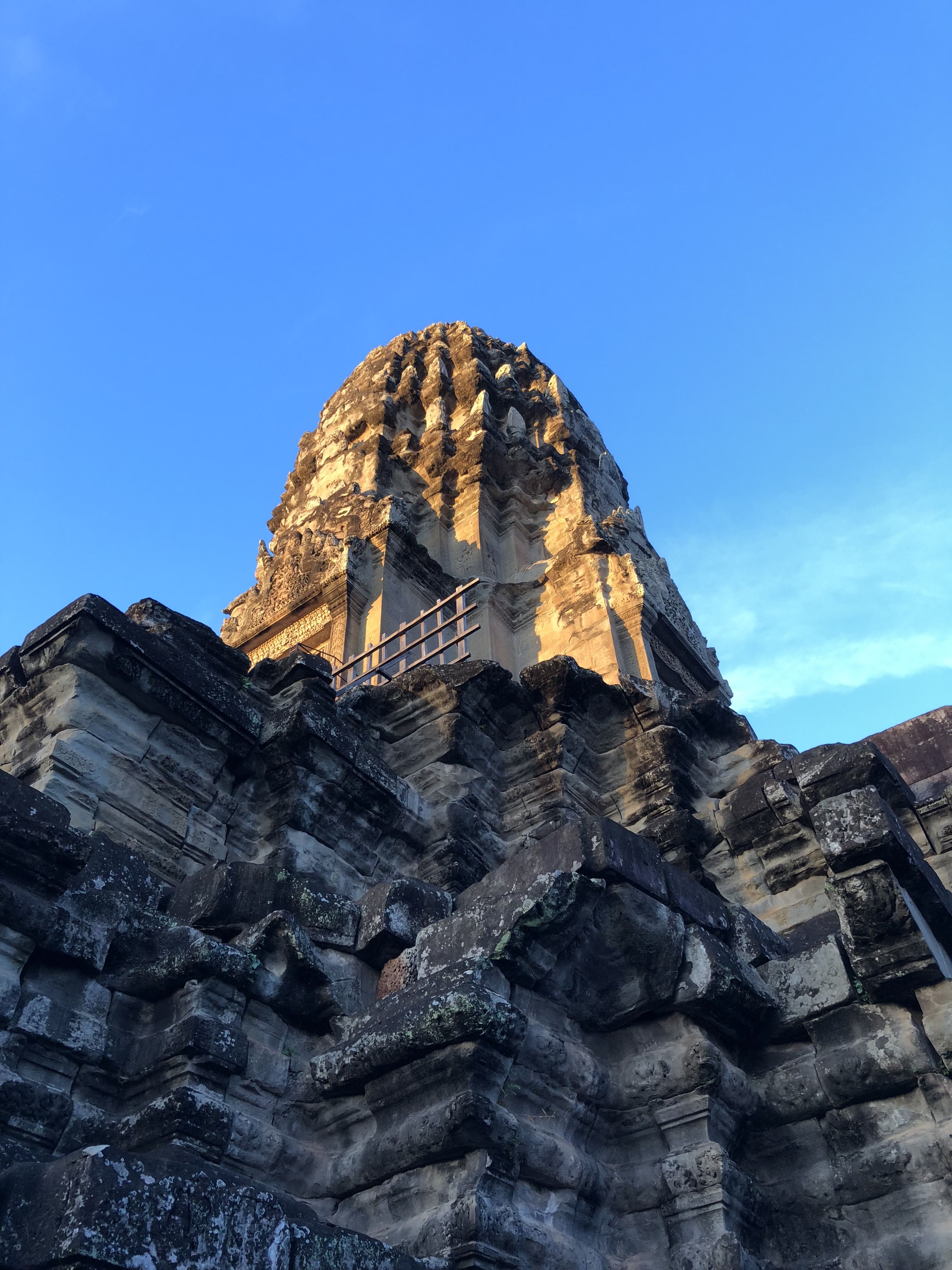 We are looking up at one of the towers of Angkor Wat. It is bathed in sunlight; below it the intricately carved walls are in shadow.