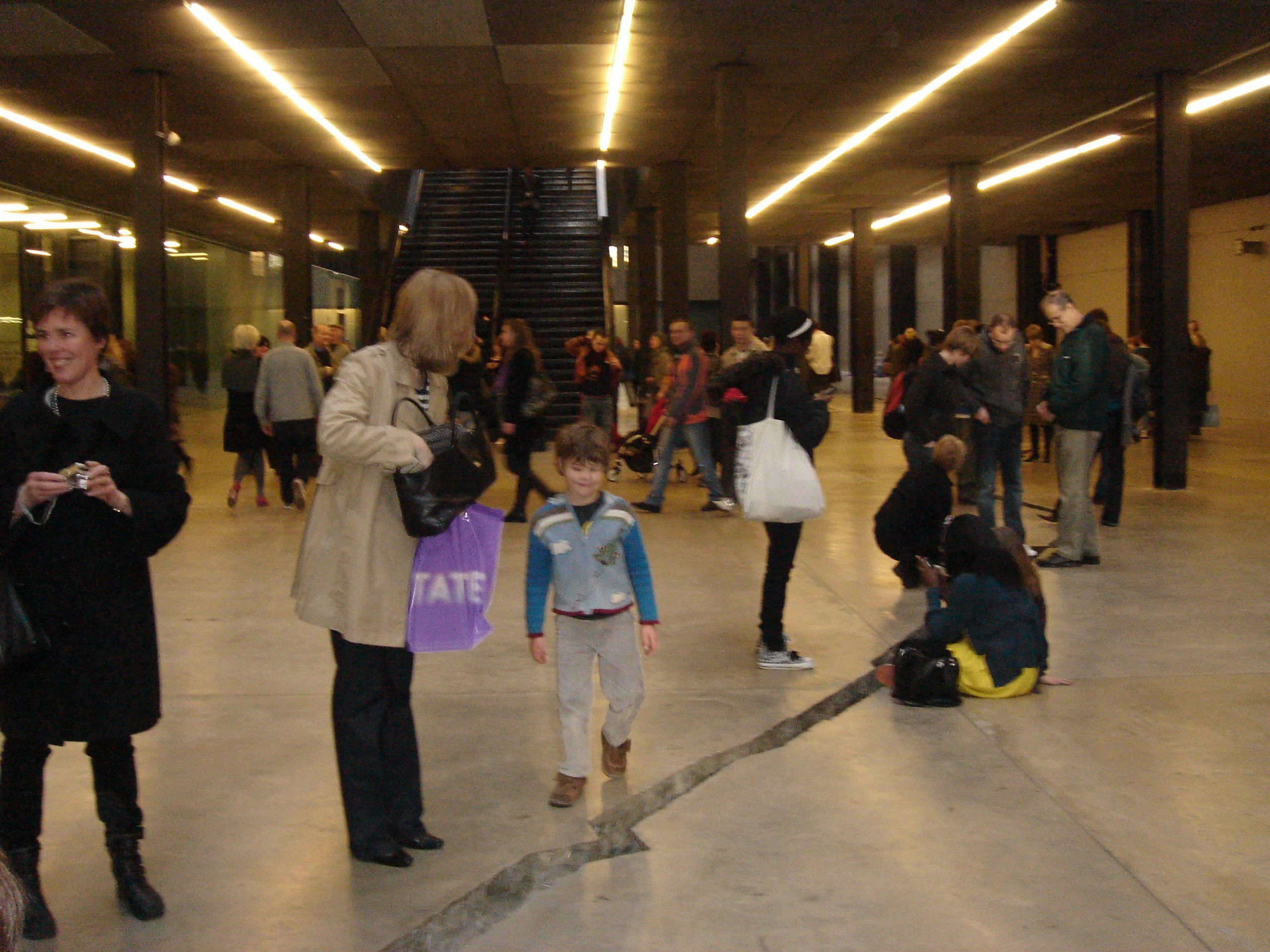 In the basement of the Tate Modern, a crack zigzags across the floor. A small boy looks at it amused. People are going in different directions.