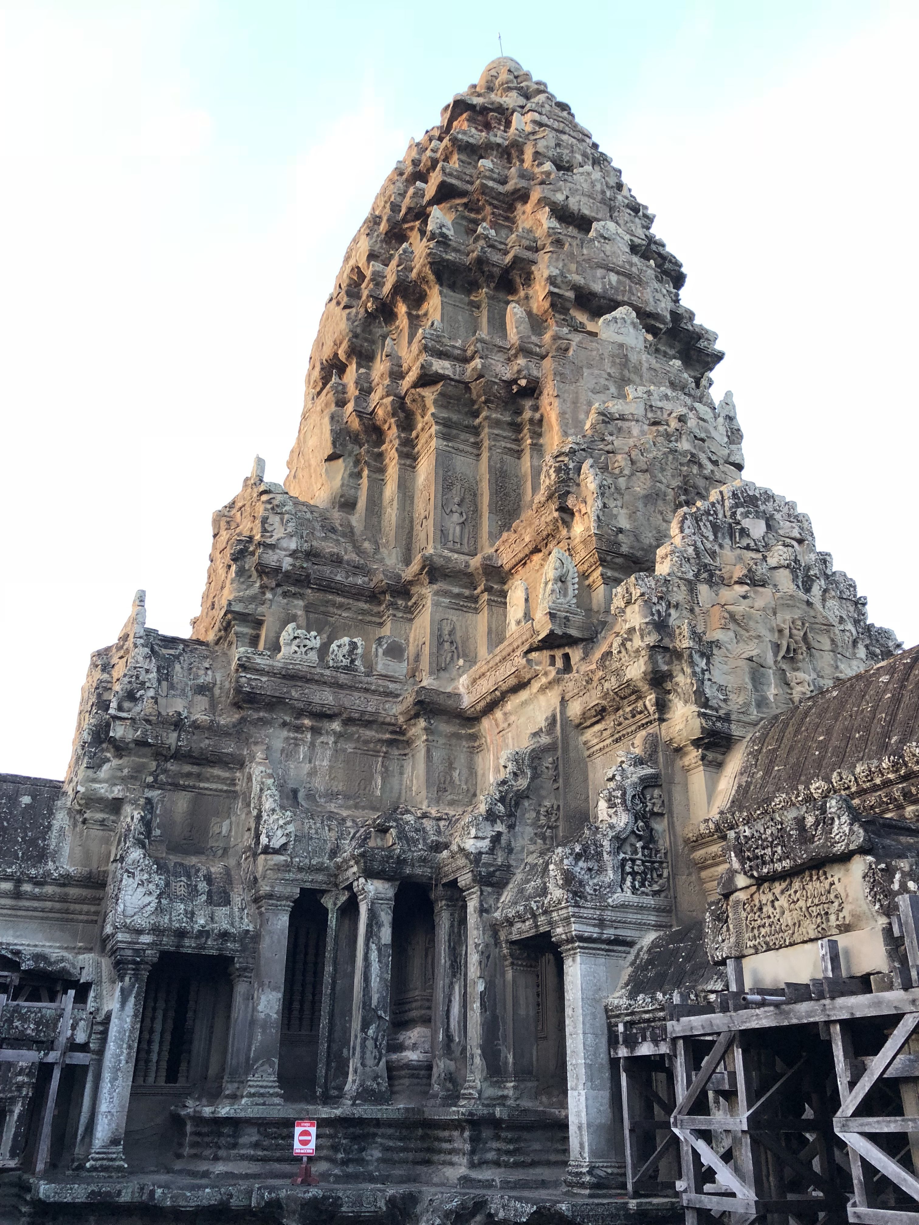 A tower at Angkor Wat. It is covered in complex carvings and at the bottom are square columns and doorways arrange in a strange and  complicated pattern.