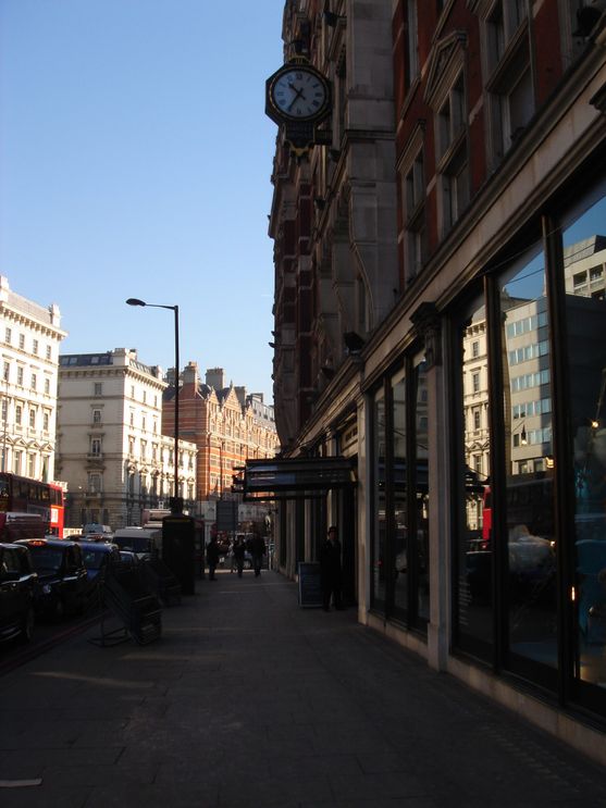 Looking along a London street with beautiful old buildings each side. Near us, on the right hand side and in shadow, is an awning marking the entrance to Harvey Nichols.