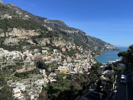 Positano on a sunny day. It consists of buildings clustered on the impossibly steep hill of a rocky promontory jutting out into the sea. The water is blue-green.