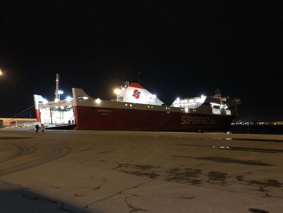 It's dark. We're looking across an expanse of concrete at a large illuminated ferry in the distance.