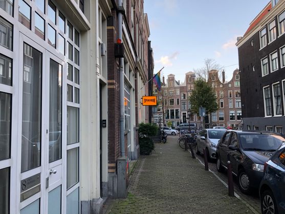 We're looking along a street in Amsterdam's old city. On the left there's a rainbow flag hanging about an illuminated sign that says Spijkerbar Amsterdam.
