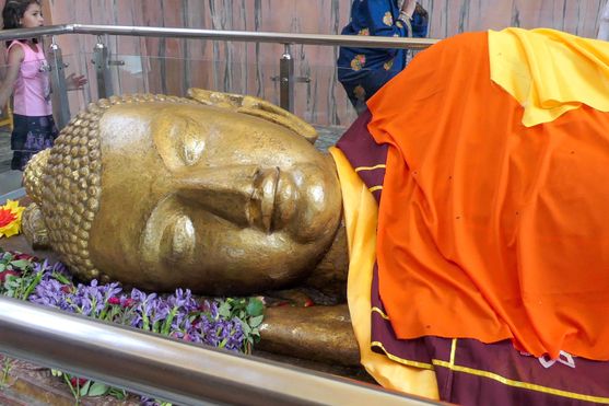 The head of a giant gold statue of the Buddha, smiling slightly. His body is draped in orange cloth