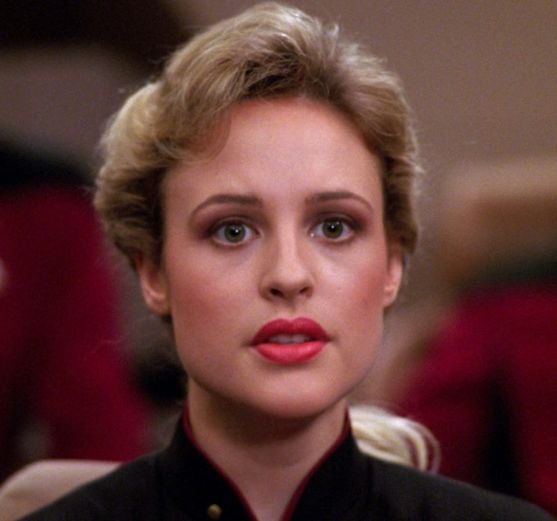 A young blond woman with striking red lipstick, seated at her station on the bridge of the Enterprise.