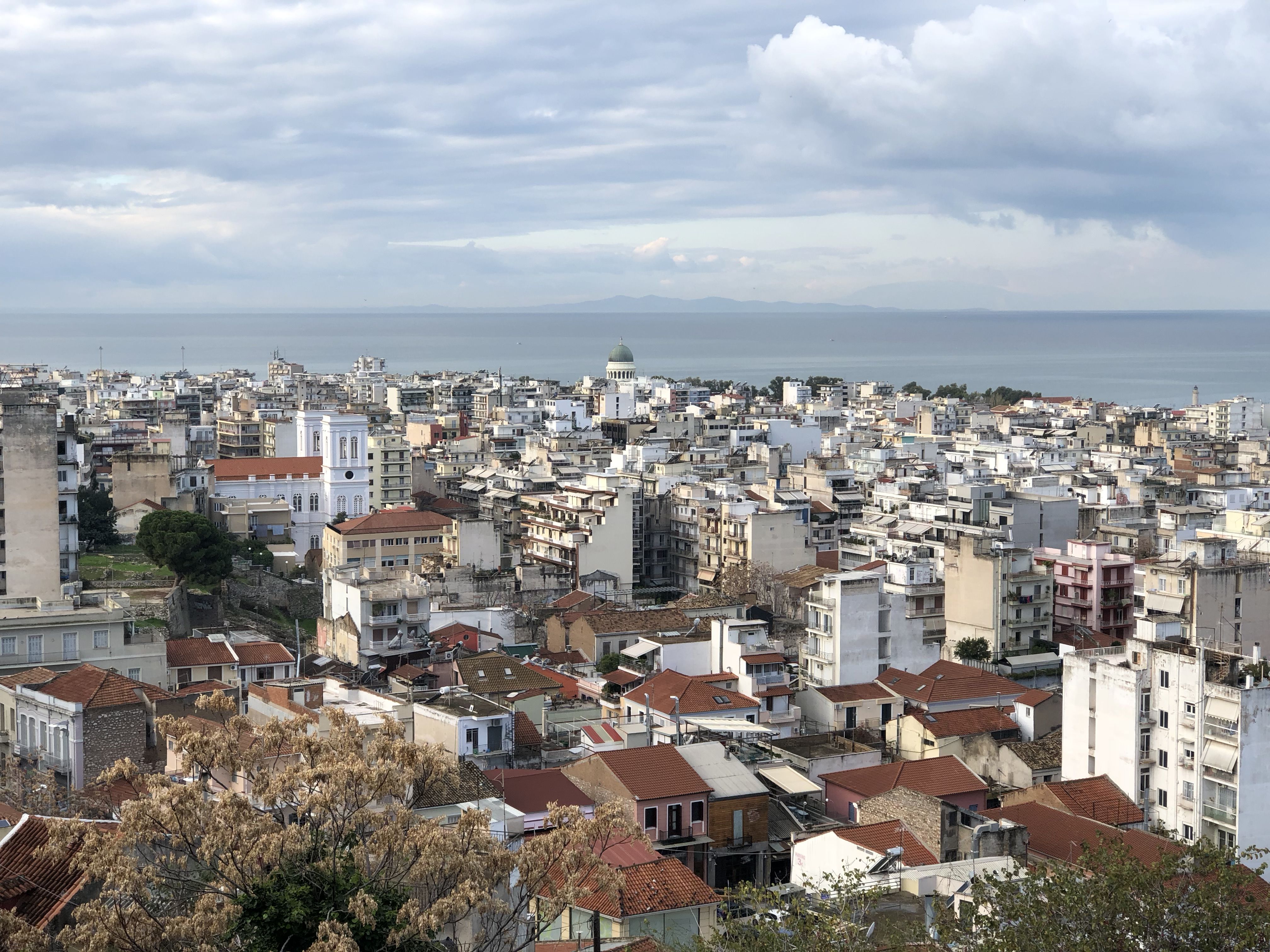 Looking out over Patras, a jumble of white buildings and red roofs until we reach the sea. In the centre, there is a church with a dome on top.