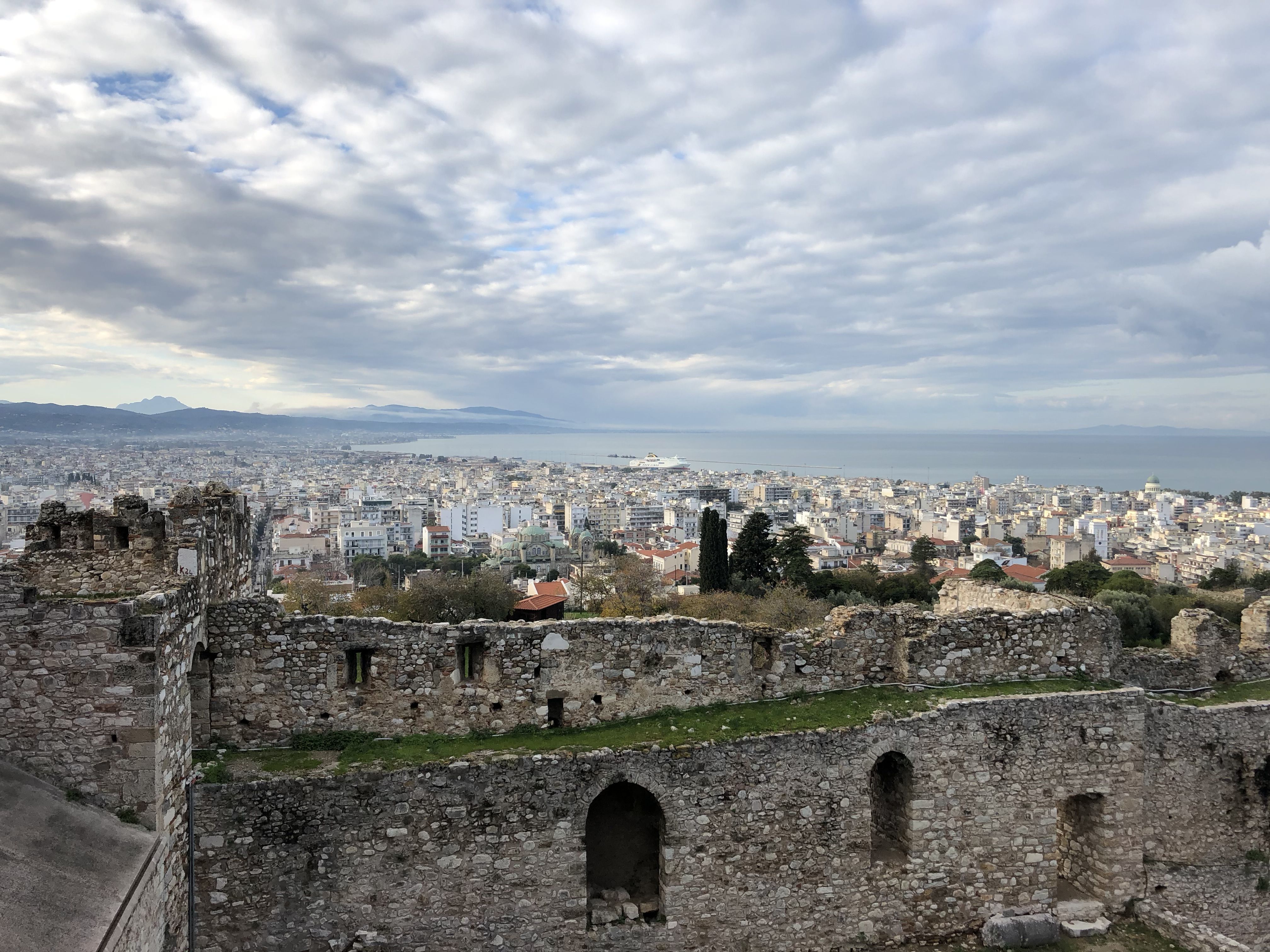 A view of Patras, across the walls and below the hill. It stretches much further into the distance than you might expect. On the right is the curve of the bay and the low clouds meet the mountains far in the distance.