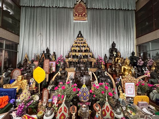 A massive altar in the form of a series of shallow steps leading up nearly more than three metres to a wall covered in silver curtains. All over the altar are statues of the Buddha, as well as fans, flowers, busts of deceased monks and other devotional items.