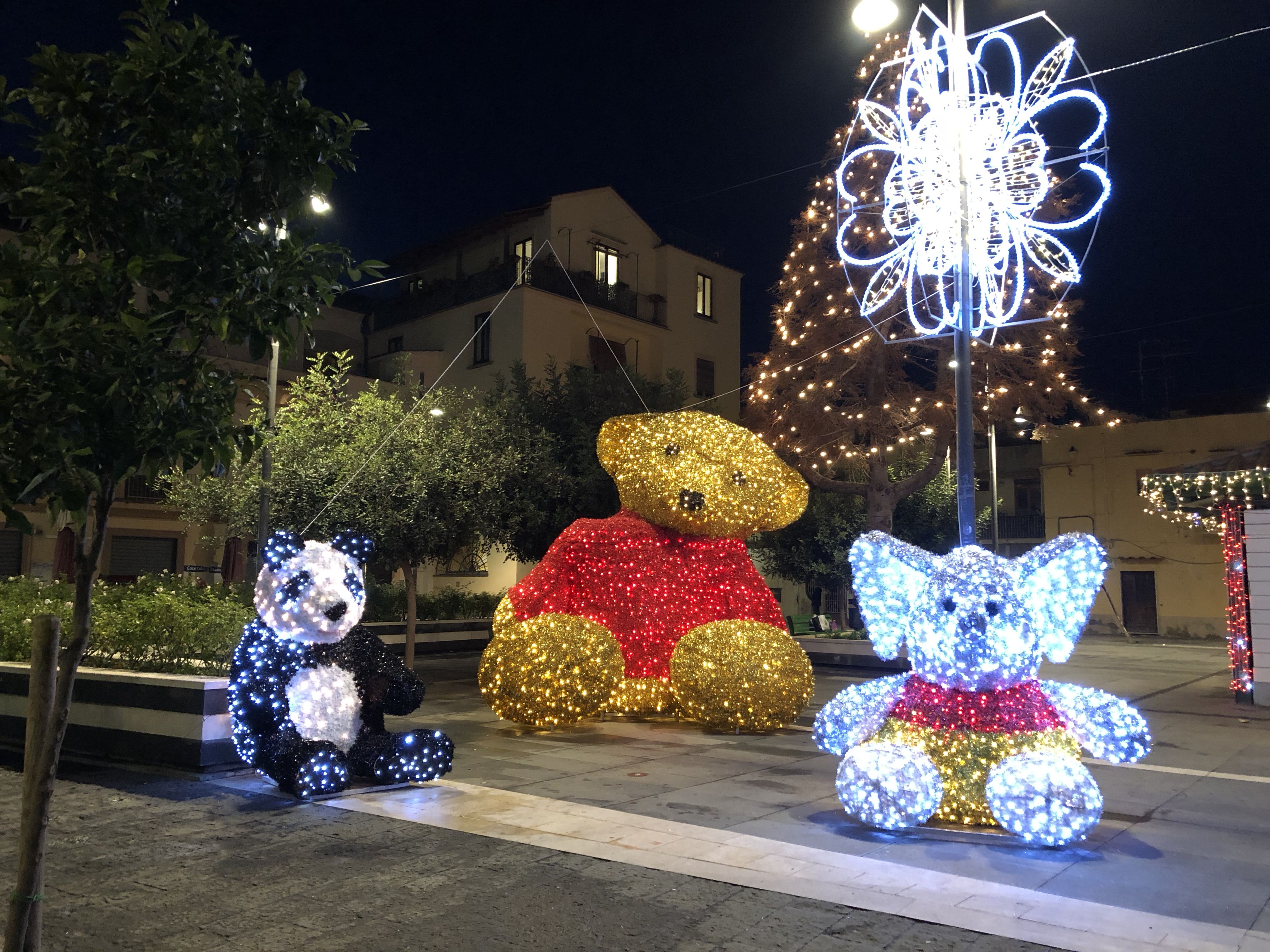 On a wide tiled walkway beside the main road through the centre  of Sorrento, sit three figures studded with Christmas lights,  taller than a person: a toy panda, a teddy bear and an elephant.