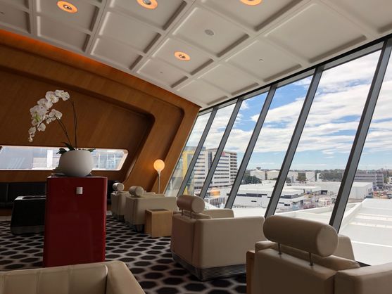 The Qantas lounge at Sydney Airport. The ceiling curves down to meet a row of glass windows looking out onto the tarmac. There's a panelled wooden wall at the end.