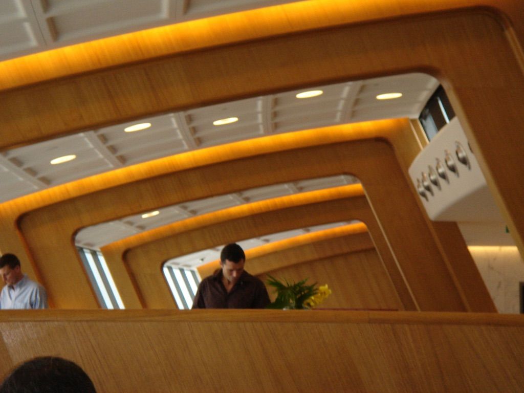 A slightly blurry picture of the inside of the Qantas lounge. A series of diagonal wooden frames leading off into the distance, with some passengers wandering around.