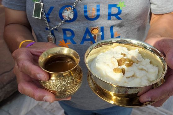 A small brass pot with honey and a larger one with a white milk/rice pudding called kheer. They are held in a man's hands.