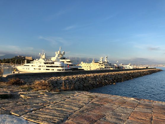 A breakwater made of stones behind which are three or four large and expensive-looking yachts.