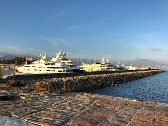 A breakwater made of stones behind which are three or four large and expensive-looking yachts.