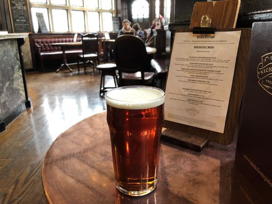 A pint of bitter on a table next to a board with a menu on it, in an old-fashioned English pub.