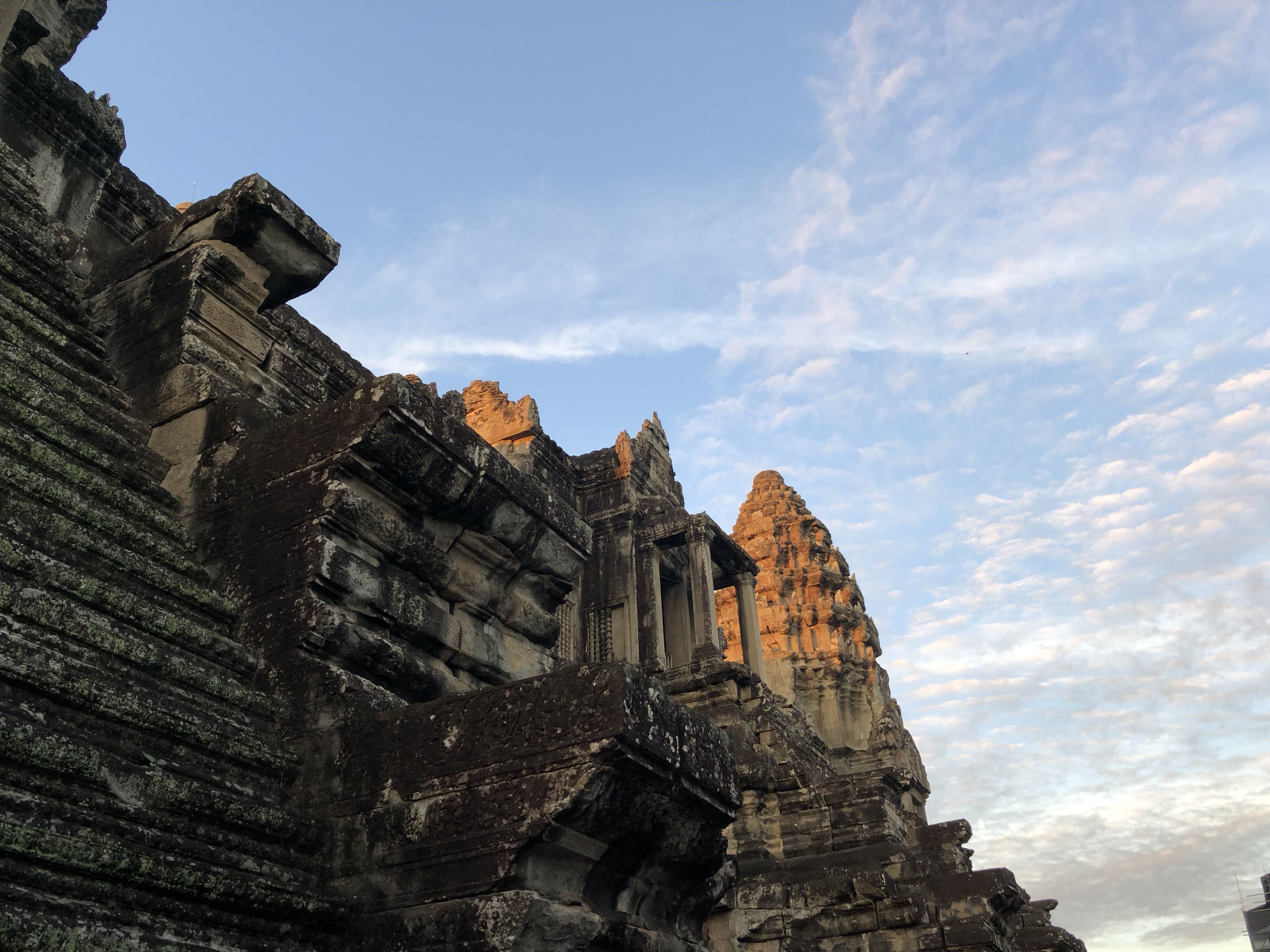 A corner of Angkor Wat, with its carved balconies in shadow. Behind them the tower is lit yellow by the early morning sunlight.