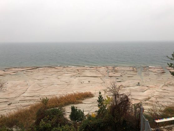 A brown rock platform extends out to the grey sea, which meets the overcast sky at a horizon shrouded in mist.