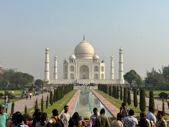 The Taj Mahal: an ornate indo-islamic building made of white marble and flanked by four towers. In front is a lawn with carefully tended paths and a long pool. And in the foreground is the inevitable crowd of people.